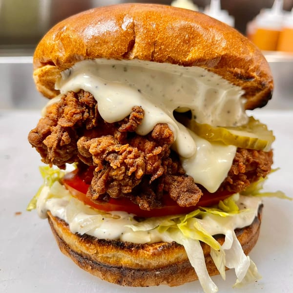 A crispy fried chicken sandwich with pickles, lettuce, tomato, and creamy sauce on a toasted bun.