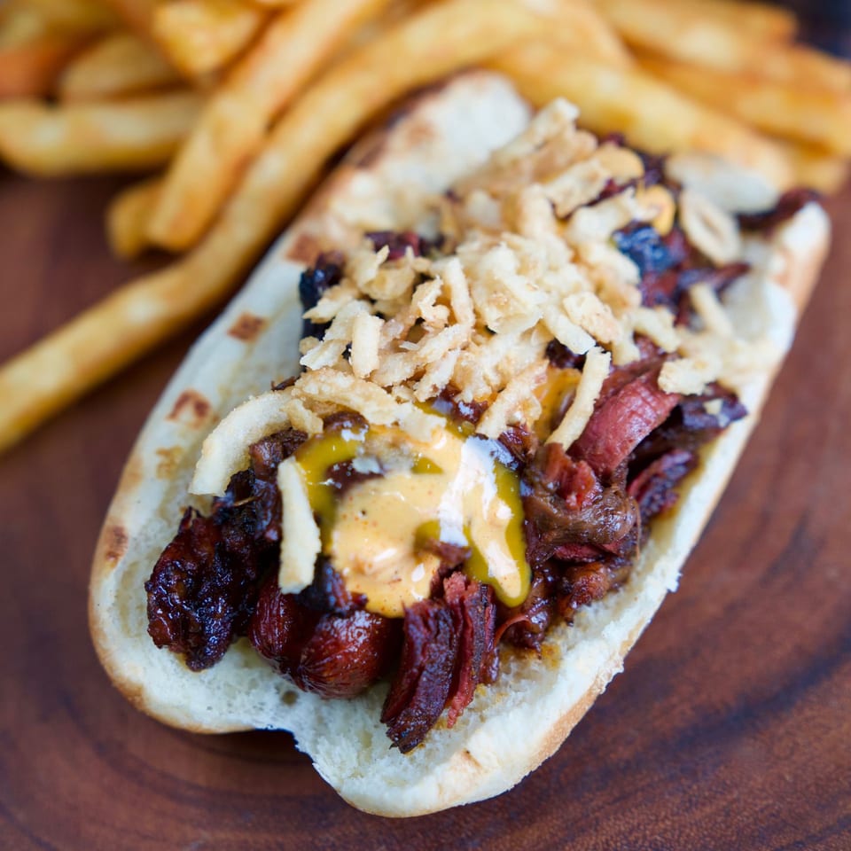 Aljoom BBQ's hot dog with pulled pork, crispy onions, and mustard, served with fries.