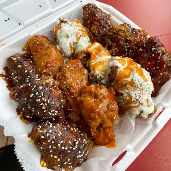 A white takeout container filled with various Aljoom BBQ chicken wings, some with white sauce.