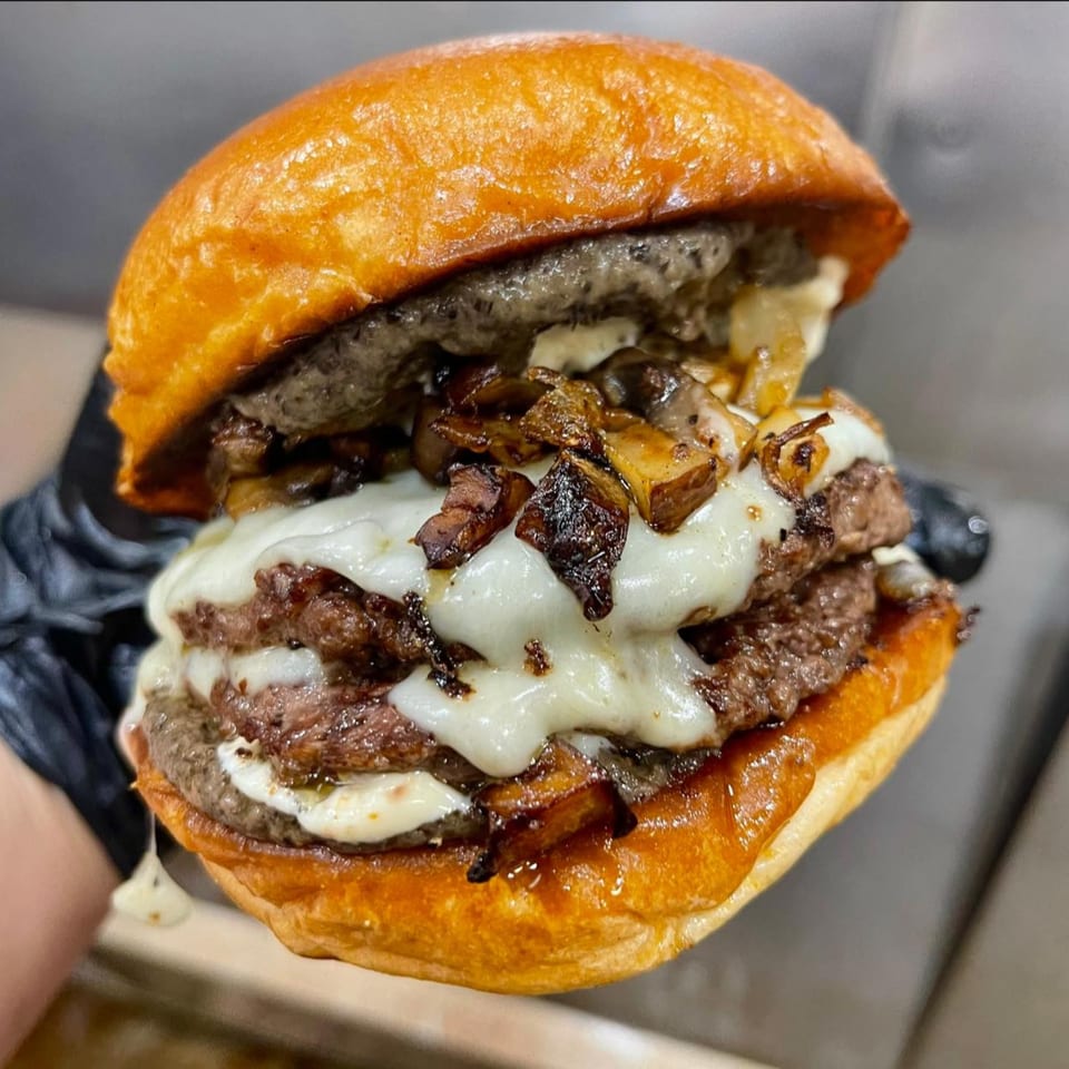 A double-patty burger with melted cheese, grilled onions, and mushrooms on a brioche bun.